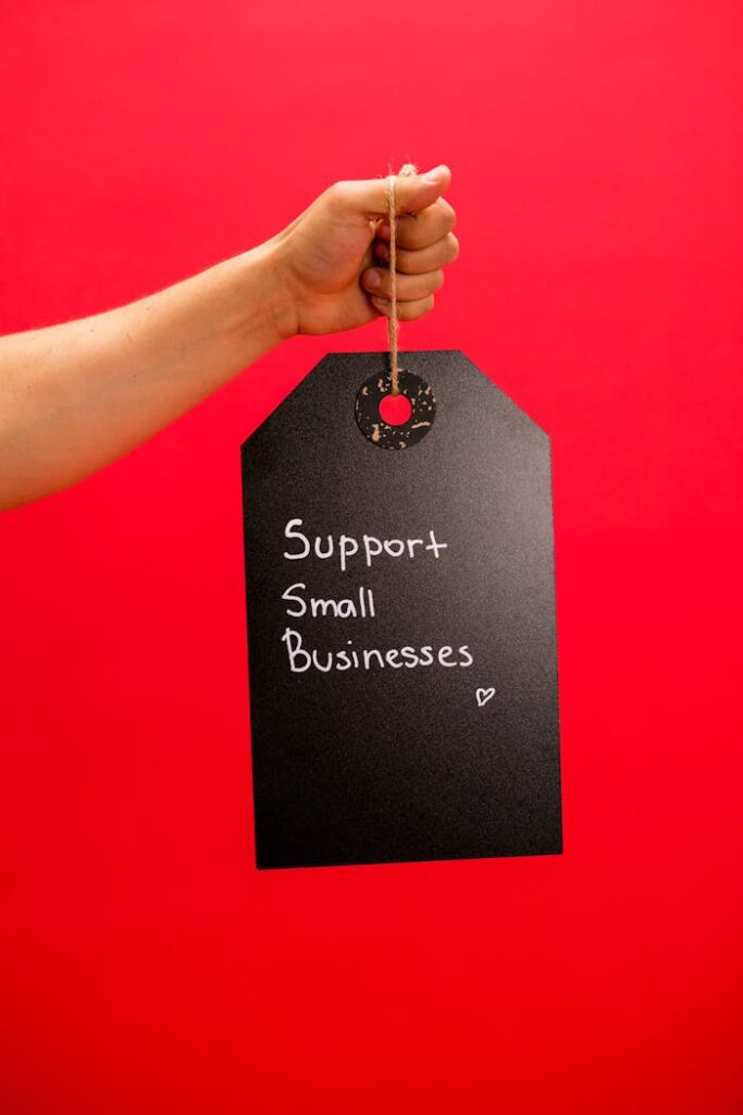 A hand holds a tag with 'Support Small Businesses' message against a vibrant red background.