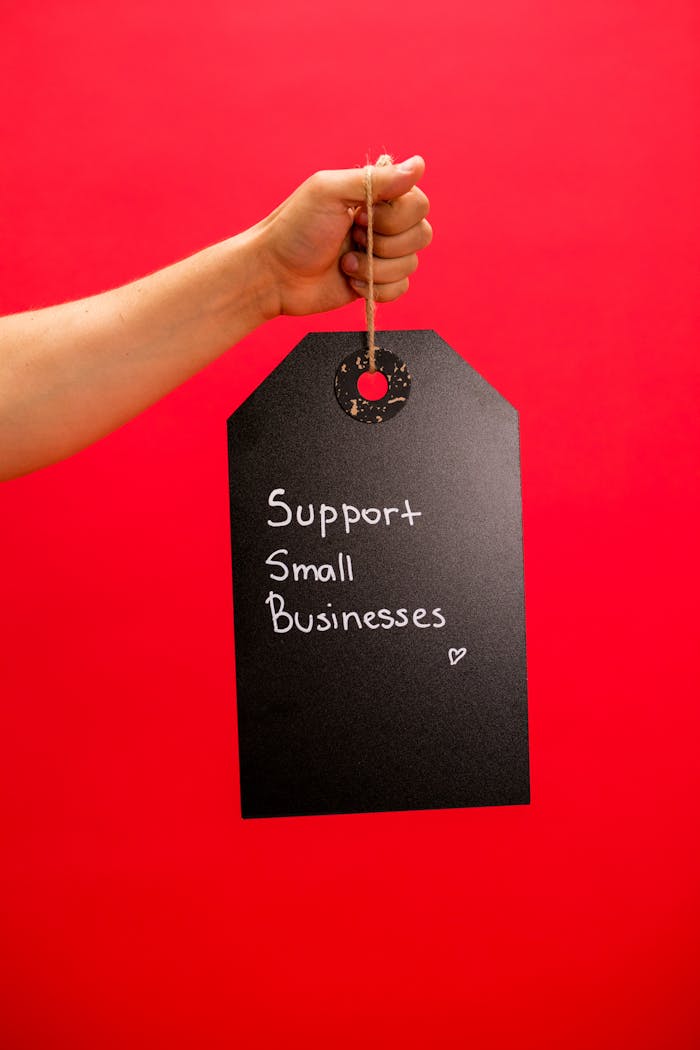 A hand holds a tag with 'Support Small Businesses' message against a vibrant red background.